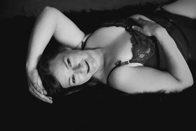 Zwart-witte foto van een lachende vrouw in lingerie, liggend op haar rug