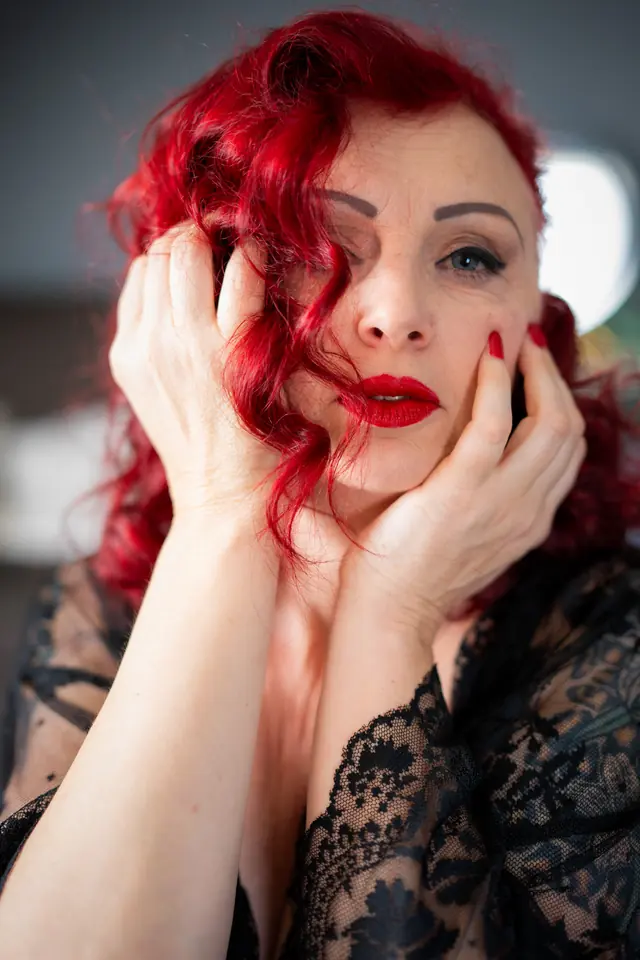 Vrouw met rood haar in zwart kant, handen langs haar gezicht