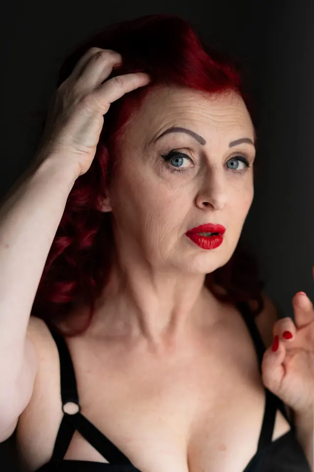 Vrouw met rood haar in een zwarte top, hand in haar haar