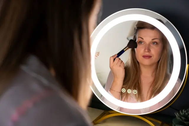 Vrouw die zich opmaakt, gefotografeerd via een ronde spiegel