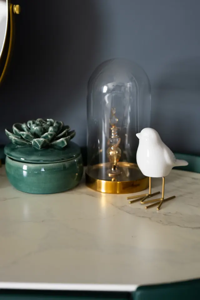 Groene kaptafel met gouden accenten, een glazen stolp en een wit vogeltje