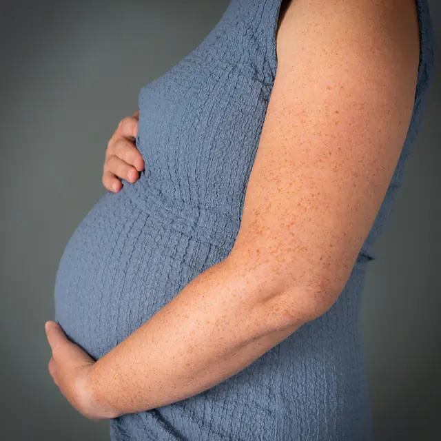 Zwangere vrouw in een blauwe jurk, in profiel met haar hand onder haar buik